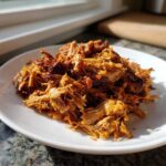 A mound of perfectly shredded and crispy Slow Cooker Carnitas piled high on a white plate.