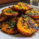 Close-up of bright orange, oven-roasted Crispy Smashed Carrot Bites sprinkled with fresh green herbs.