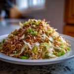 A mound of Crunchy Asian Ramen Noodle Salad featuring ramen noodles, cabbage, green onions, and a crunchy topping.