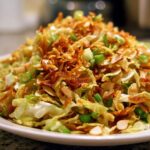 A close-up of a serving of Crunchy Asian Ramen Noodle Salad, topped with crispy fried noodles and sliced almonds.
