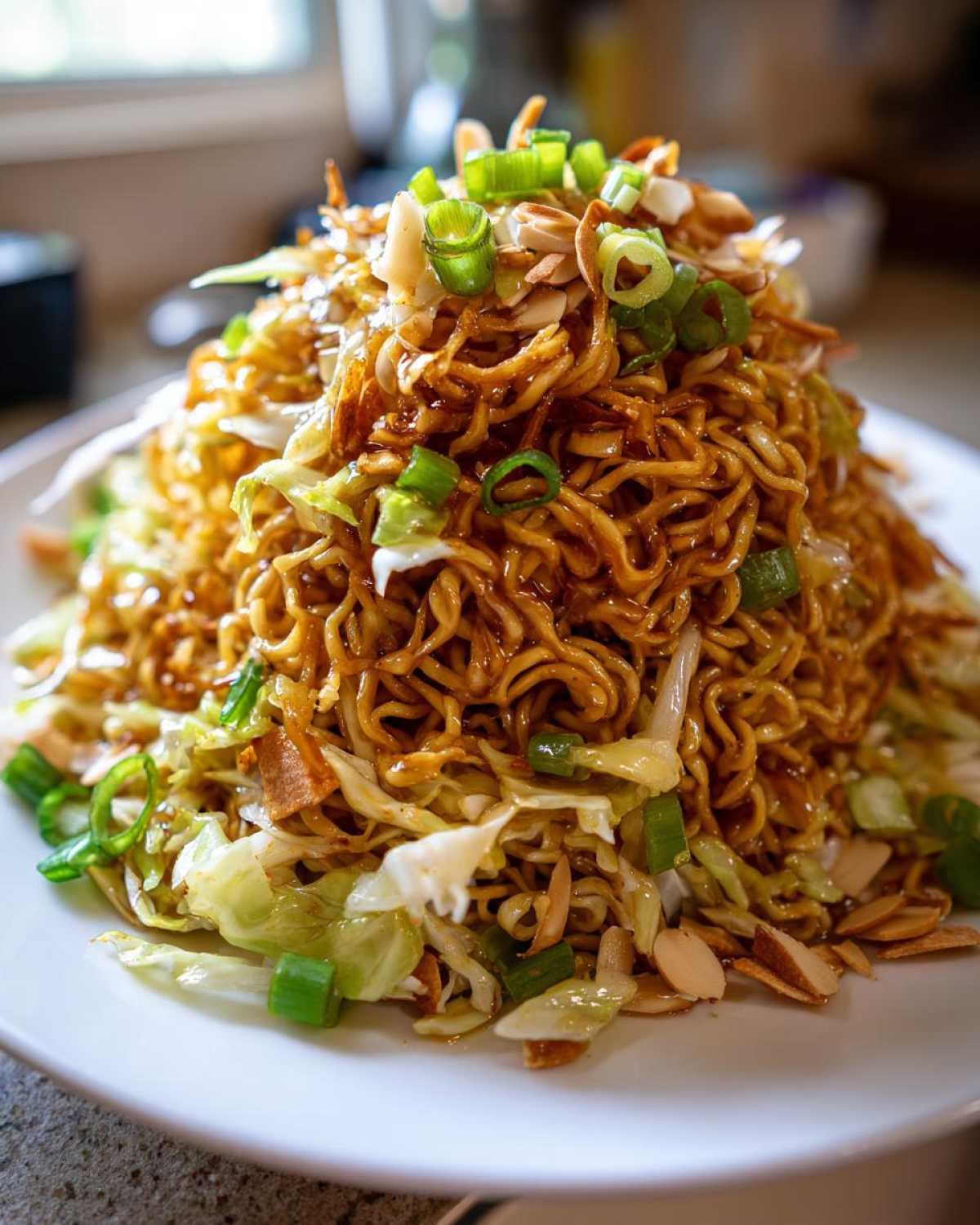 A mound of Crunchy Asian Ramen Noodle Salad tossed in dressing, topped with sliced almonds and green onions.