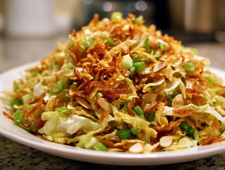 A close-up of a serving of Crunchy Asian Ramen Noodle Salad, topped with crispy fried noodles and sliced almonds.