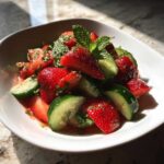 Close-up of a refreshing Cucumber Strawberry Salad featuring sliced strawberries, cucumber chunks, and fresh mint leaves.