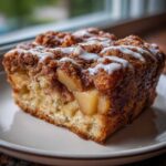 A close-up of a moist slice of Easy Amish Apple Fritter Bread topped with cinnamon streusel and white icing.