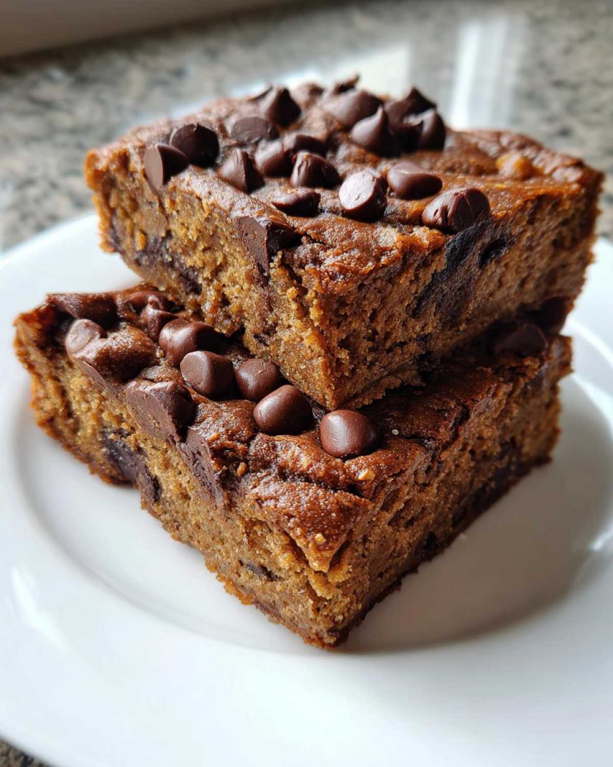 Two stacked squares of Easy Bakerystyle Chocolate Chip Banana bars topped with melted chocolate chips on a white plate.