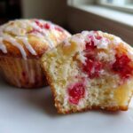 Close-up of Easy Bakerystyle Fresh Strawberry Muffins, one whole and one cut open showing bright red fruit inside and a white glaze.