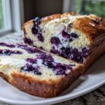 A loaf of Easy Blueberry Cream Cheese Bread, sliced to show the rich swirls of cream cheese and bursting blueberries inside.