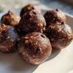 Close-up of several Easy Chocolate Peanut Butter Banana Bites, dark brown and studded with oats and mini chocolate chips, on a light plate.