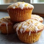 A stack of four Easy Classic Lemon Poppy Seed Muffins topped with a thick white lemon glaze and zest.