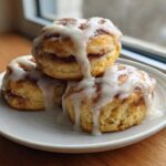 Three Easy Heavenly Cinnamon Bun Scones stacked on a plate, dripping with vanilla icing.