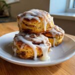 A stack of three Easy Heavenly Cinnamon Bun Scones covered in thick white icing, resting on a white plate.