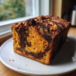 A close-up of a slice of Easy Moist Cinnamon Swirl Pumpkin bread showing rich orange crumb and dark cinnamon swirl.