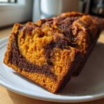 Close-up of a slice of Easy Moist Cinnamon Swirl Pumpkin bread showing the orange pumpkin cake marbled with dark cinnamon swirl.