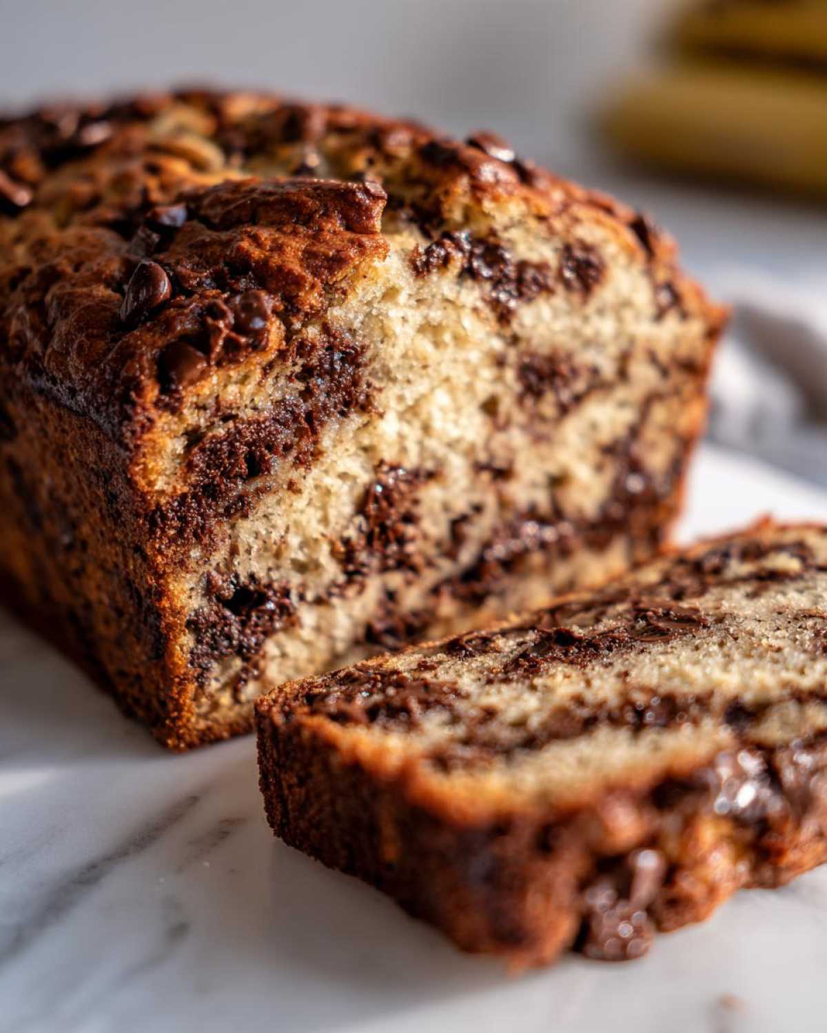 Close-up of Easy Mouthwatering Banana Bread Chocolate loaf with a slice cut, showing moist interior and melted chocolate chips.
