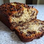 A freshly baked loaf of Easy Mouthwatering Banana Bread Chocolate with a slice cut off, showing moist interior.