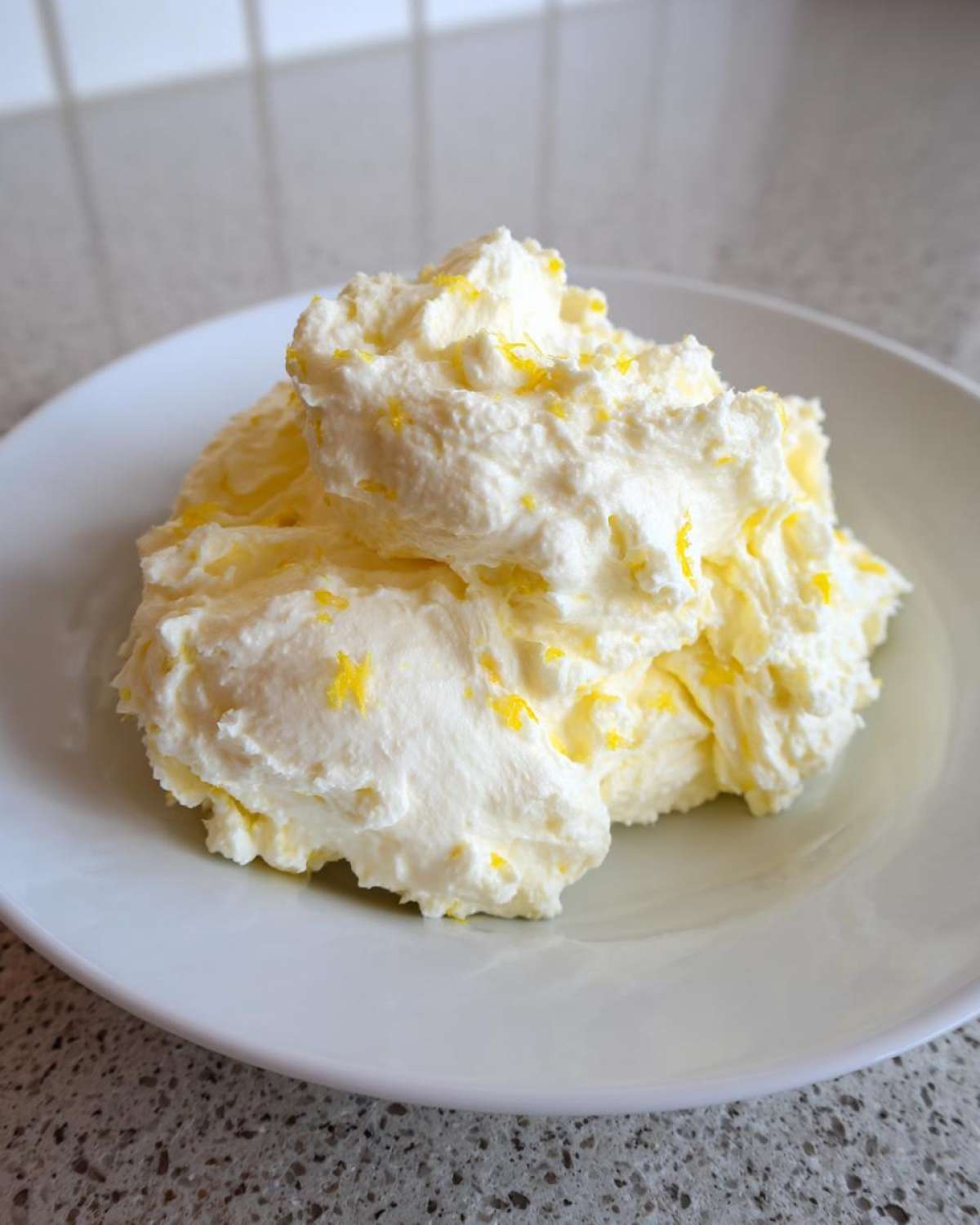 A mound of fluffy Easy Soft Lemon Cream Cheese topped with bright yellow lemon zest on a white plate.