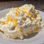 A mound of fluffy Easy Soft Lemon Cream Cheese topped with bright orange lemon zest in a white bowl.
