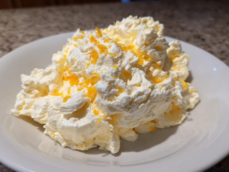 A mound of fluffy Easy Soft Lemon Cream Cheese topped with bright orange lemon zest in a white bowl.