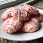 A stack of pink and white swirled Easy Strawberry Lemonade Cookies drizzled with white icing on a white plate.
