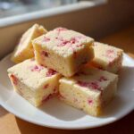 Stack of buttery Easy Strawberry Shortbread Cookies cut into squares on a white plate.