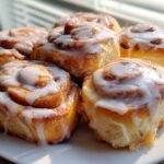 A close-up of several freshly baked, soft Breakfast Rolls topped with thick white icing.