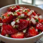 Close-up of vibrant, chunky Strawberry Salsa featuring diced strawberries, white onion, and green herbs in a white bowl.