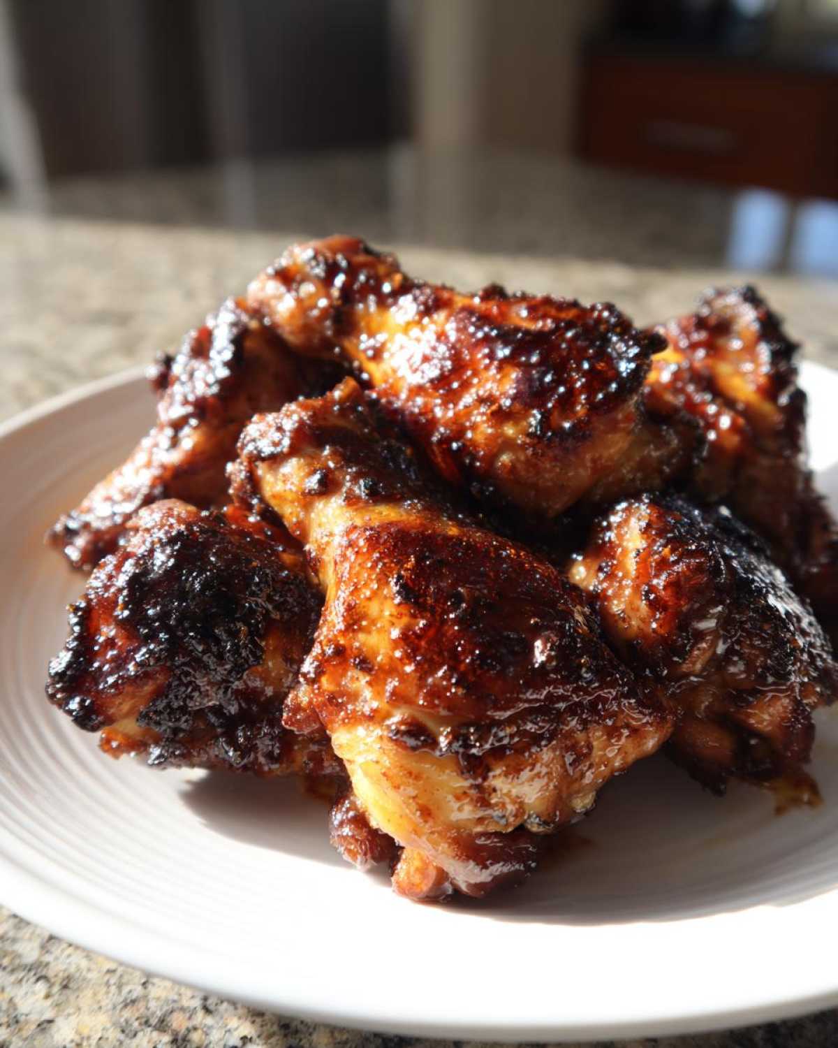 A close-up of several glossy, caramelized Huli Huli Chicken drumettes piled on a white plate.