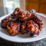 Close-up of several pieces of sticky, caramelized Huli Huli Chicken piled on a white plate.