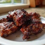 Close-up of several pieces of sticky, caramelized Huli Huli Chicken served on a white plate.