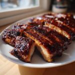 Close-up of sticky, glazed Oven Baked Ribs cut into individual portions on a white plate.
