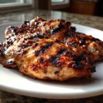 Two pieces of perfectly charred and glazed Grilled Cuban Chicken resting on a white plate.