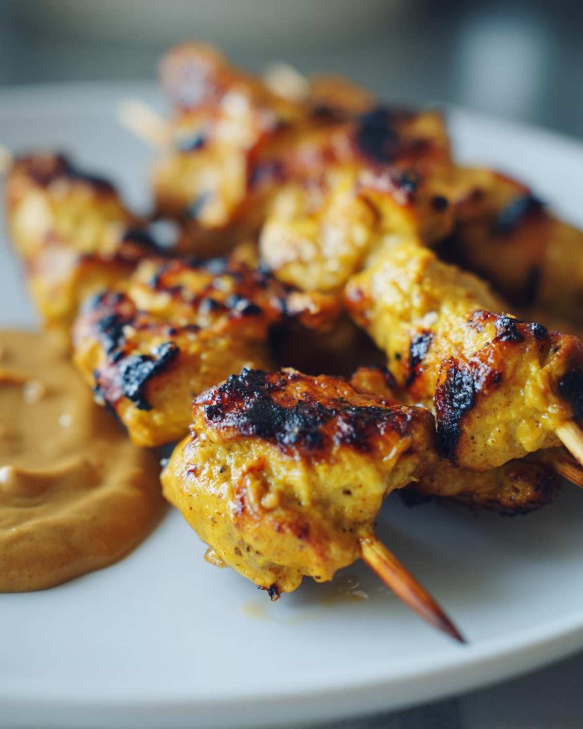 Close-up of beautifully charred Grilled Thai Chicken Skewers served with a side of creamy peanut sauce on a white plate.