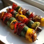 Three skewers of colorful, charred Grilled Vegetable Kabobs BBQ featuring zucchini, bell peppers, and onions on a white plate.