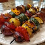 Close-up of two skewers loaded with colorful, charred Grilled Vegetable Kabobs BBQ, including zucchini, red onion, and peppers.