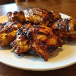 Close-up of several pieces of juicy, caramelized Grilled Vietnamese Chicken with distinct char marks on a white plate.
