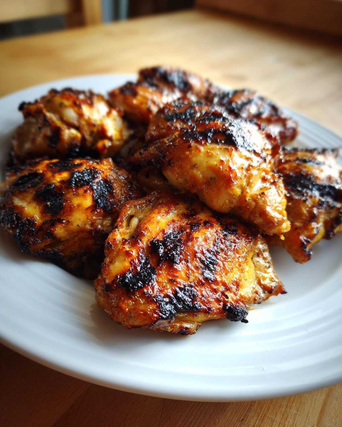 A close-up of several pieces of juicy Grilled Vietnamese Chicken with dark char marks on a white plate.