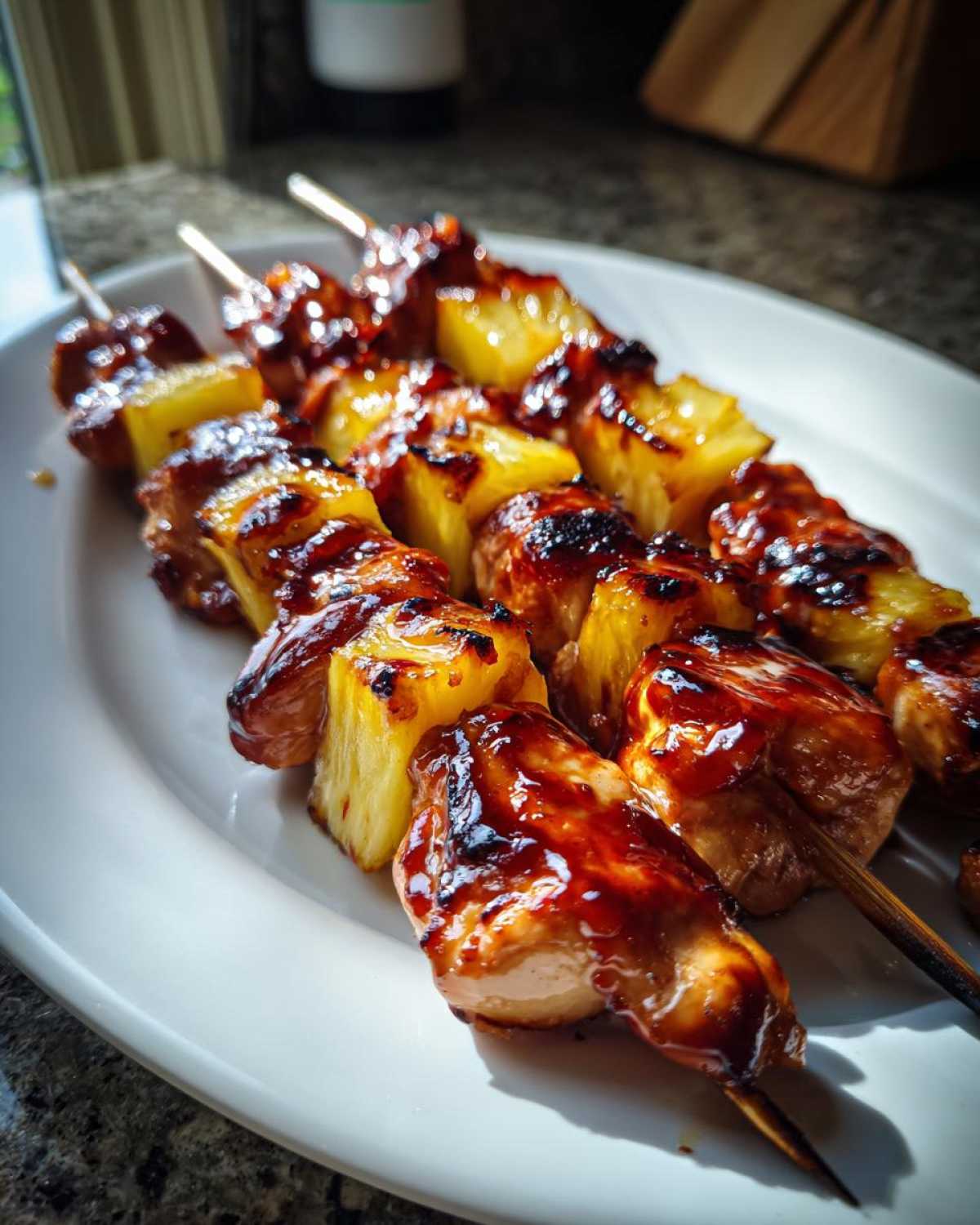 Close-up of grilled Hawaiian Teriyaki Chicken Kabobs Pineapple skewers glistening with dark teriyaki glaze on a white plate.