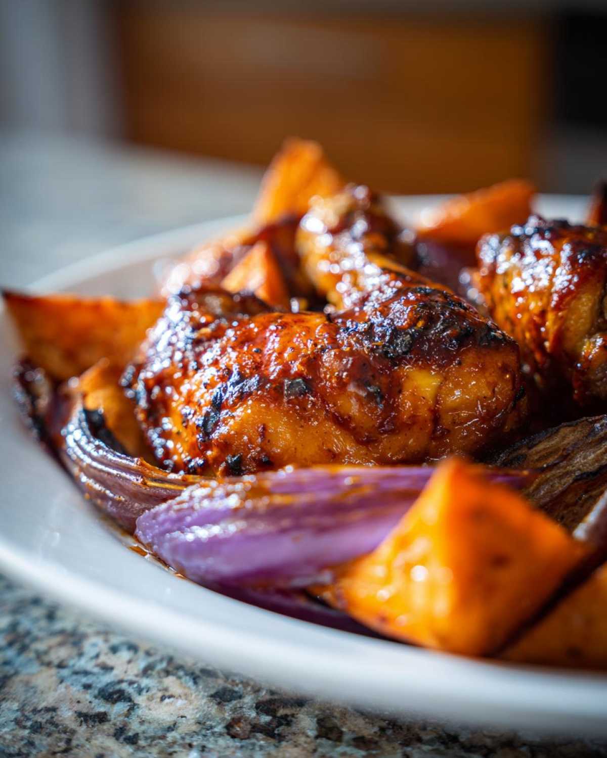 Close-up of glazed Honey Harissa Chicken drumsticks served with roasted sweet potatoes and red onions.