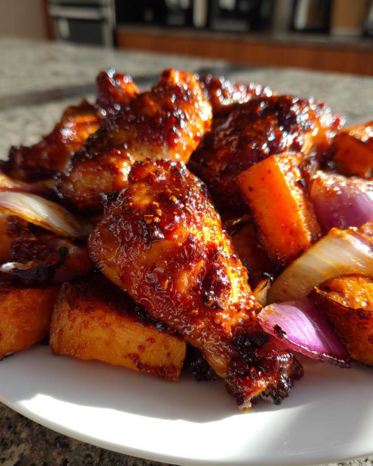 Close-up of glossy, glazed Honey Harissa Chicken drumsticks served with roasted sweet potatoes and red onions.
