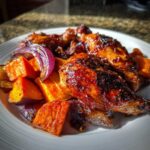 Close-up of glazed Honey Harissa Chicken pieces served with roasted sweet potatoes and red onion wedges.