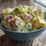 Close-up of creamy Jamaican Jerk Potato Salad mixed with red onion and green onions in a teal bowl.