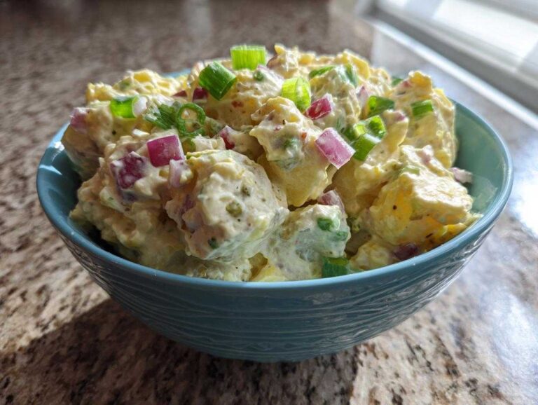 Close-up of creamy Jamaican Jerk Potato Salad mixed with red onion and green onions in a teal bowl.