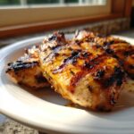 Close-up of perfectly cooked Grilled Cuban Chicken breasts with caramelized, charred grill marks on a white plate.