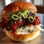 A close-up of a delicious Korean BBQ Chicken Sandwich featuring glazed chicken, coleslaw, and sesame seeds on a brioche bun.