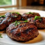 Five perfectly grilled, juicy Lebanese Kafta patties garnished with fresh parsley on a white plate.