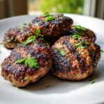Close-up of grilled Lebanese Kafta patties garnished with fresh parsley on a white plate.