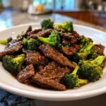 A close-up of glossy, saucy Low Carb Mongolian Beef Recipe mixed with bright green broccoli florets served in a white bowl.