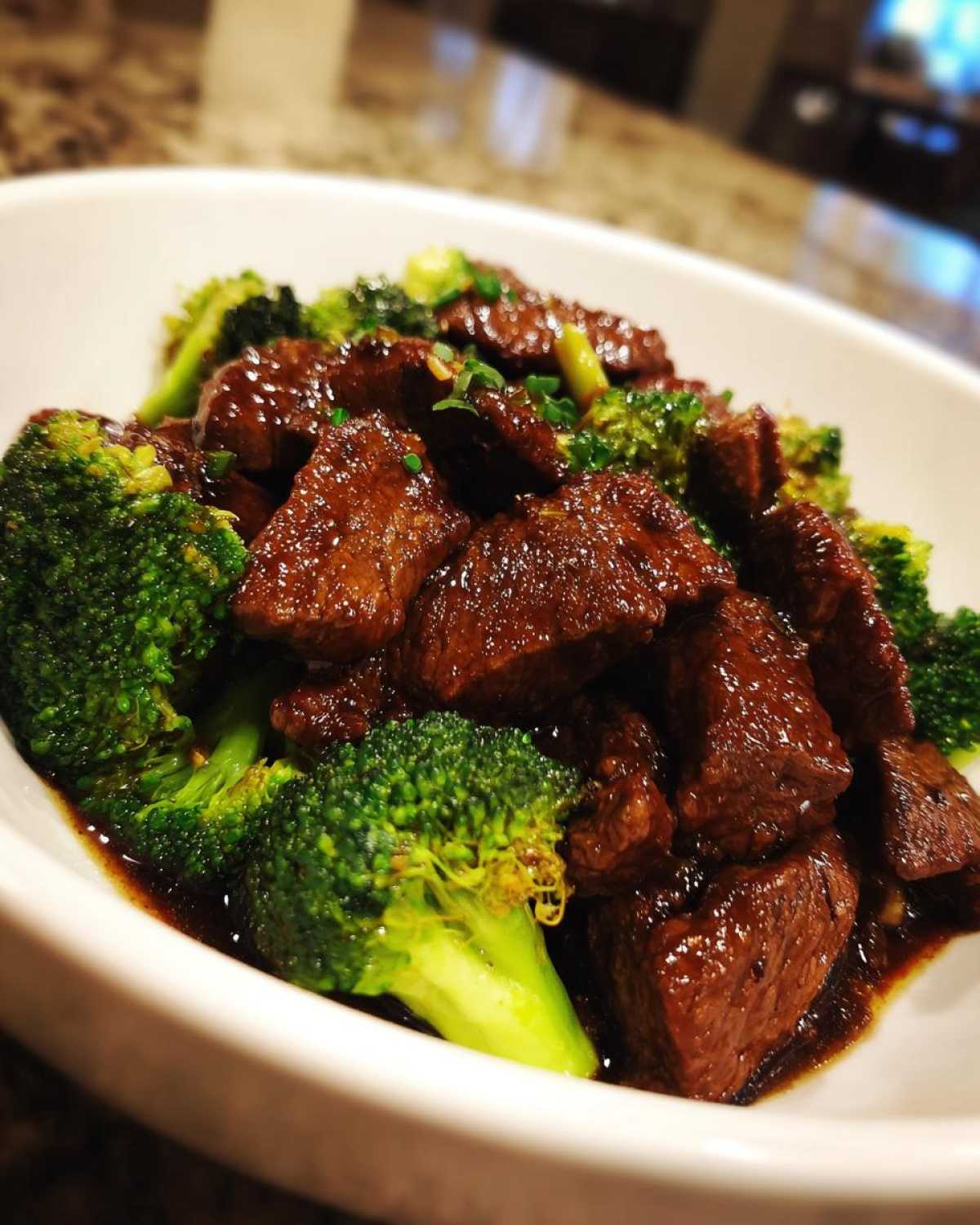 Close-up of tender beef chunks coated in dark sauce served with bright green broccoli florets in a white bowl, part of the Low Carb Mongolian Beef Recipe.