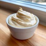 A small white bowl filled with thick, creamy, and perfectly piped Lowcarb Garlic Aioli, set on a wooden surface.