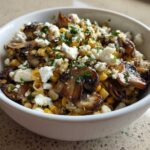 Close-up of Mexican Street Corn Salad MushroomSalus featuring charred corn, mushrooms, and crumbled white cheese in a white bowl.